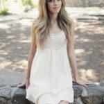 Portrait of a young woman in a white dress sitting outdoors on a sunny day.